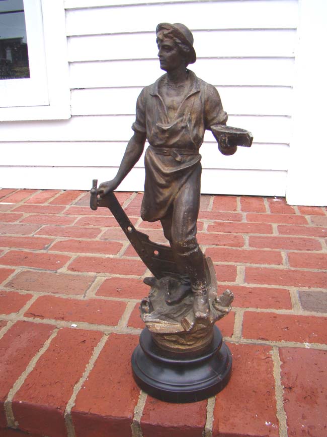 A 19th century metal sculpture of a shipbuilder holding a small ship in one hand and his tool in the other. Circa 1883. — image 2