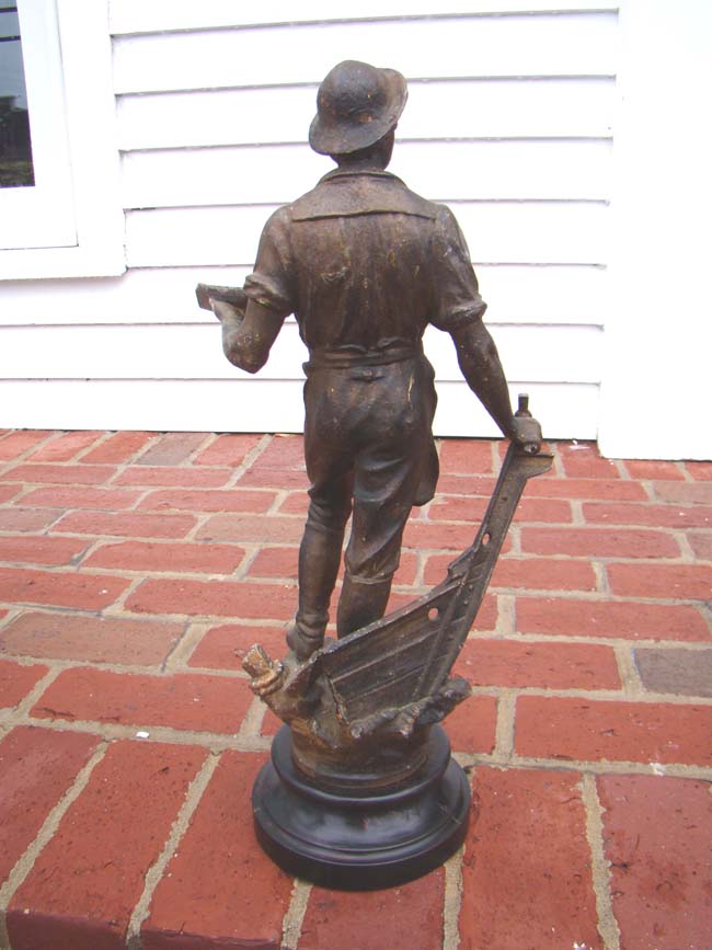 A 19th century metal sculpture of a shipbuilder holding a small ship in one hand and his tool in the other. Circa 1883. — image 3
