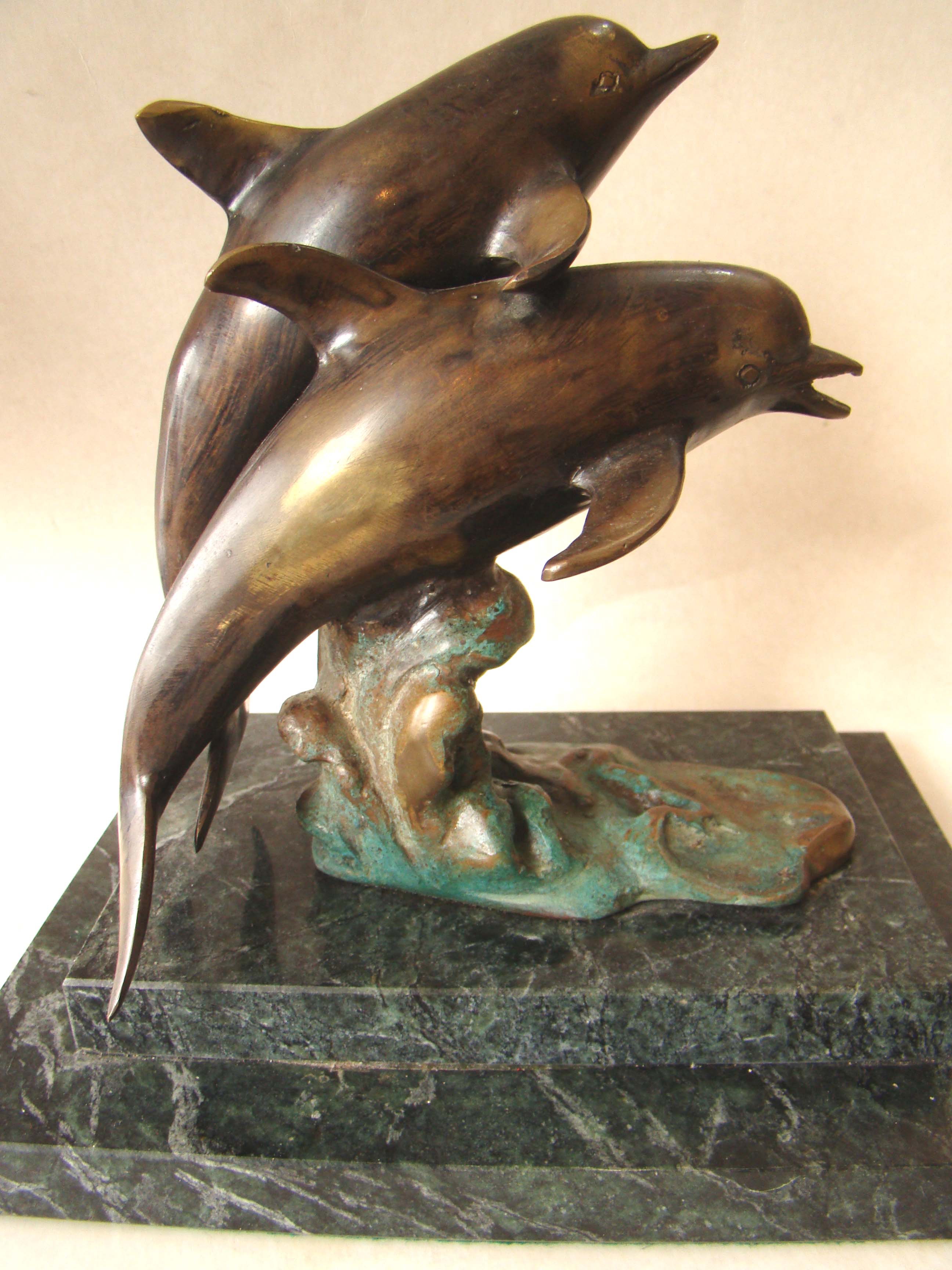 A wonderful solid bronze sculpture depicting two dolphins mounted on a green marble base