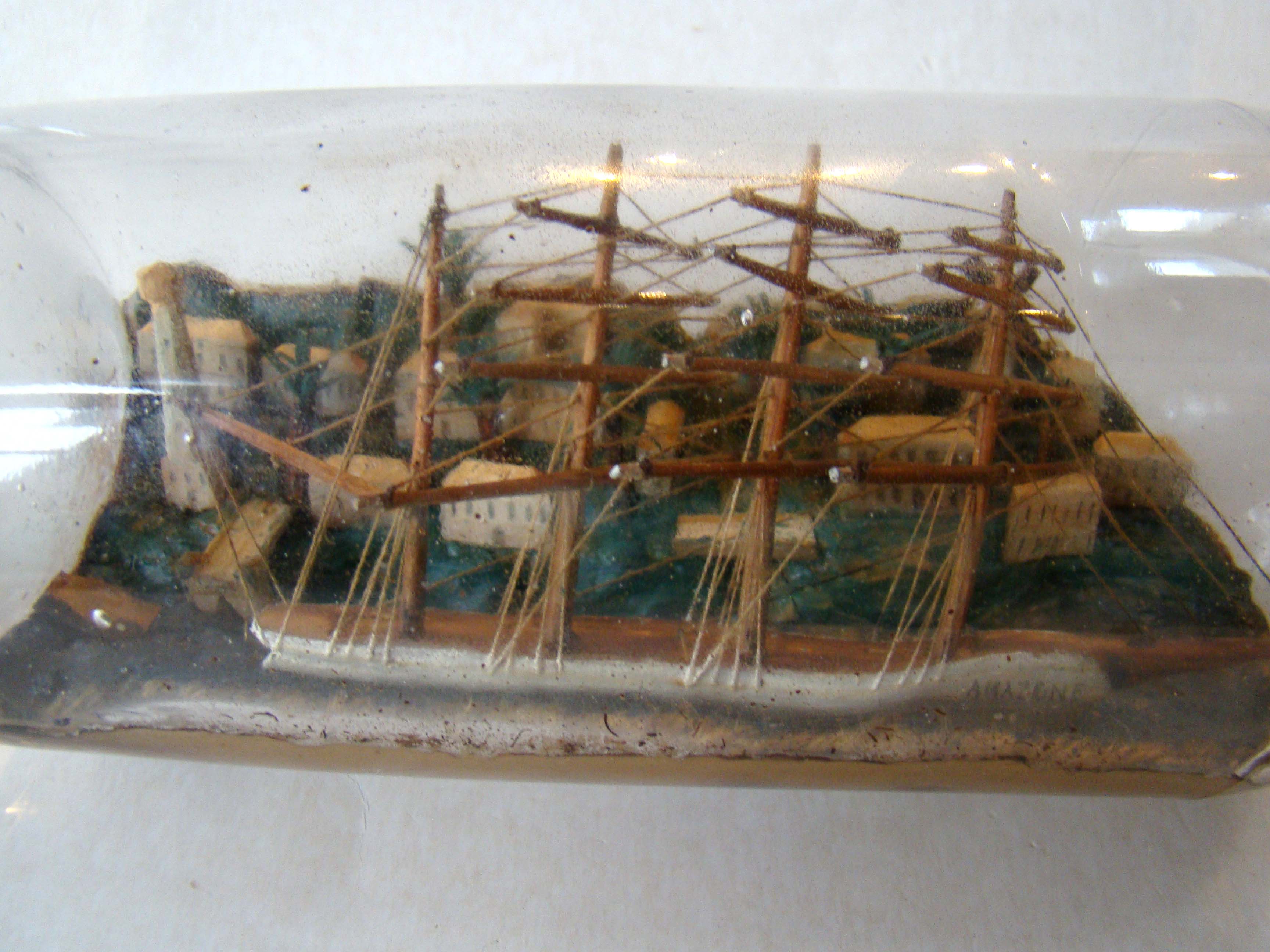 A four-masted ship-in-a bottle with a highly detailed and extensive village scene in the background circa 1890-1900.