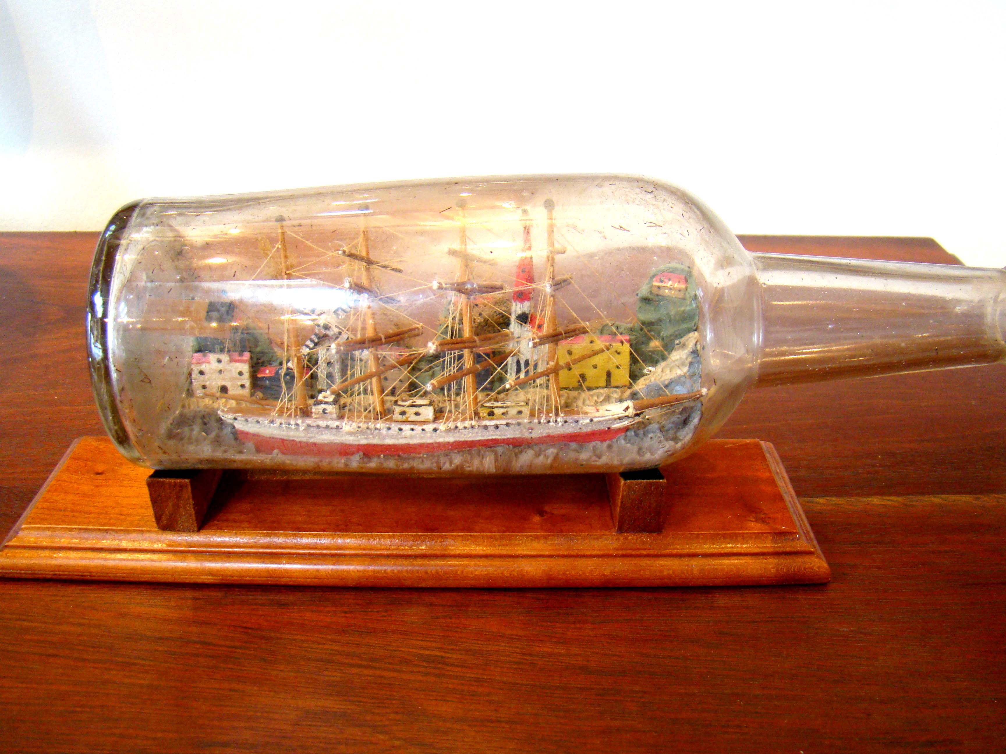 A fine vintage four-masted ship-in a bottle flying the American flag  with a charming village in the background circa 1900-1920  