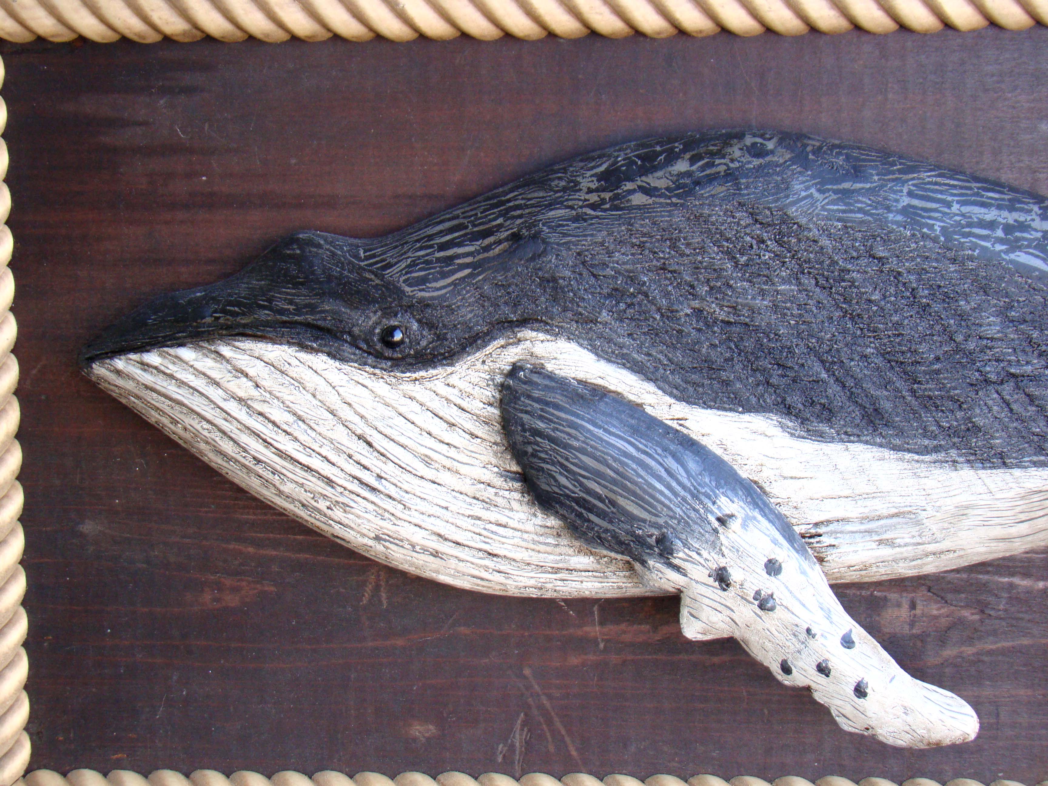 A wonderful vintage carved whale mounted on an antique backboard with rope border
