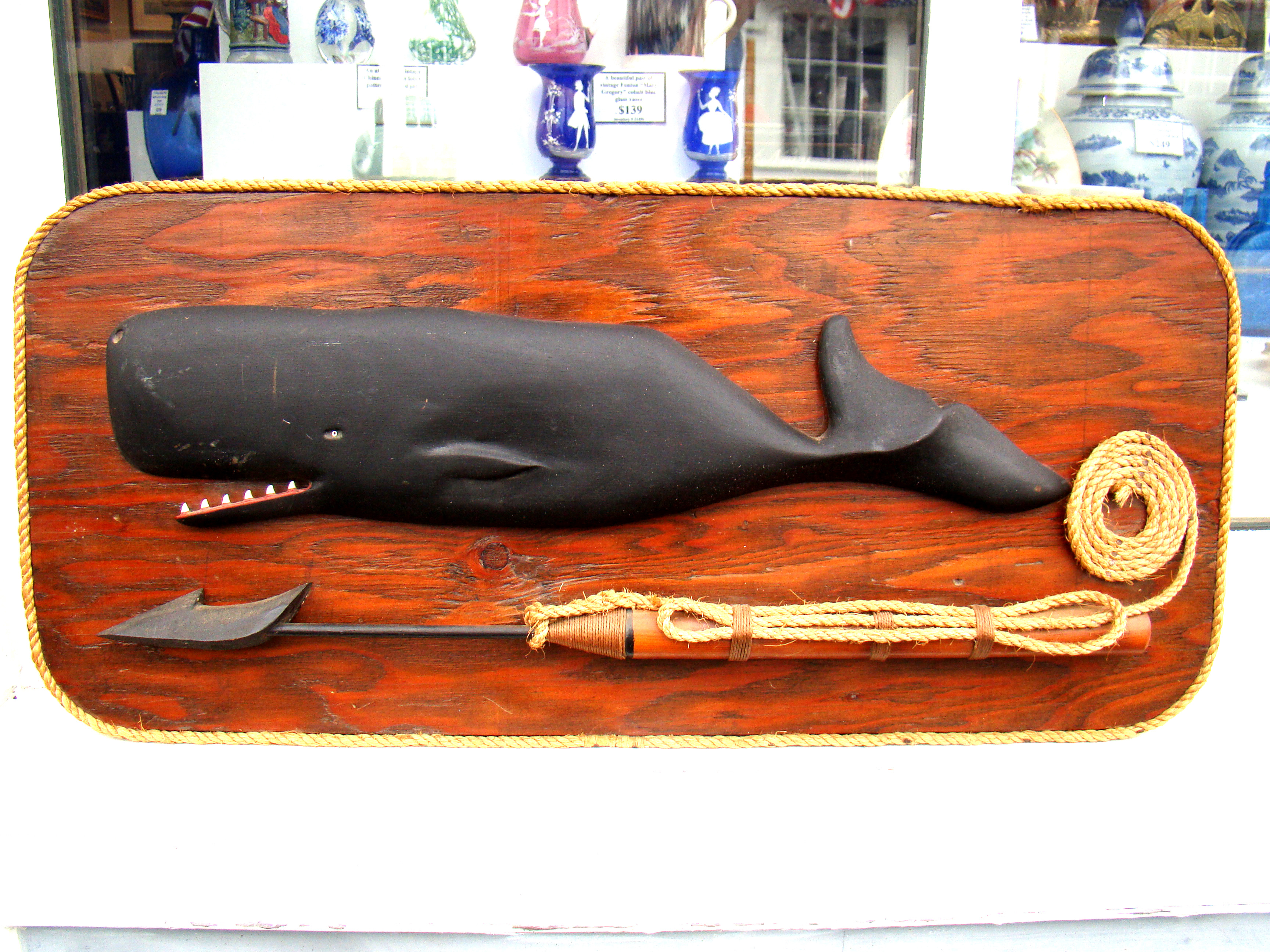 A well-executed carving of a sperm whale mounted on a backboard along with a harpoon